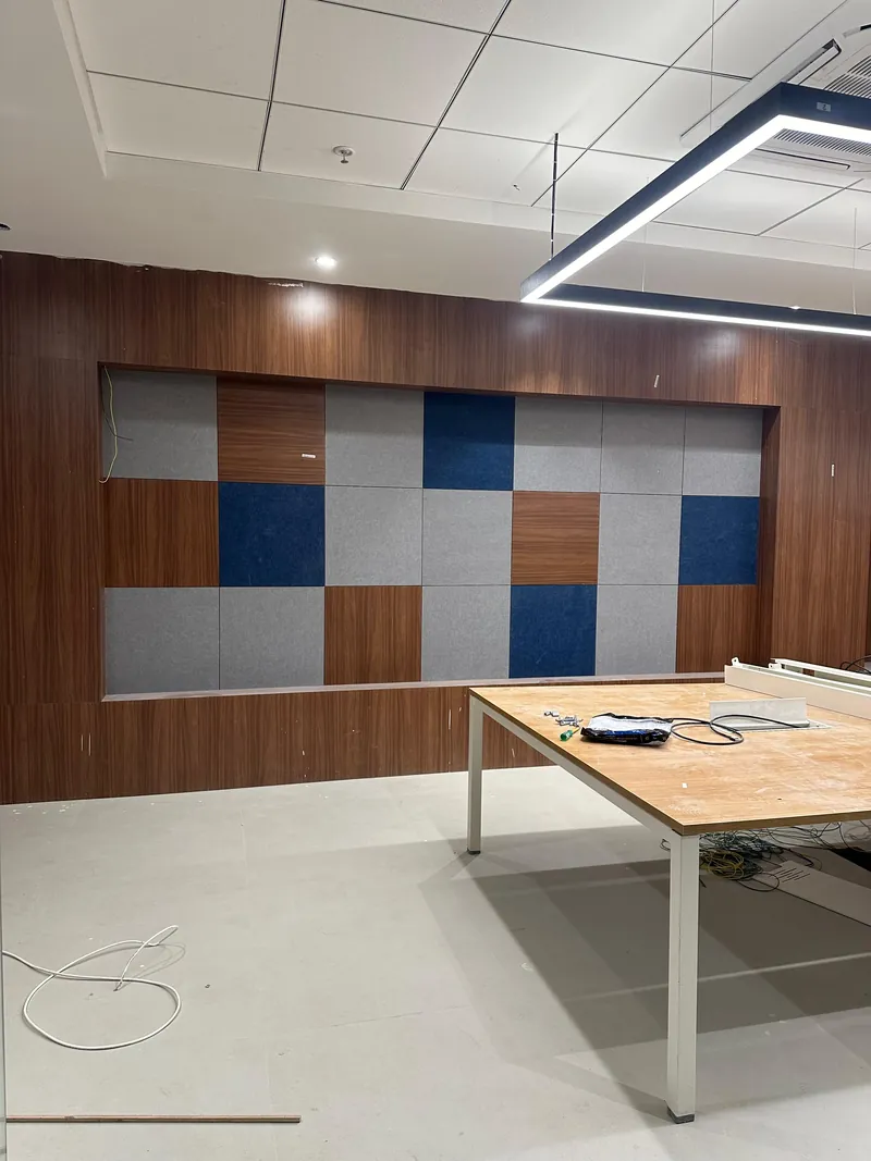 Office workstation area with checkered acoustic wall panels and wood paneling under construction.