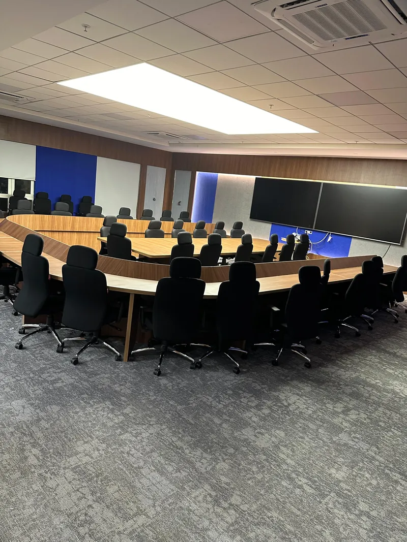 Boardroom with curved conference table, executive chairs and twin wall-mounted screens.