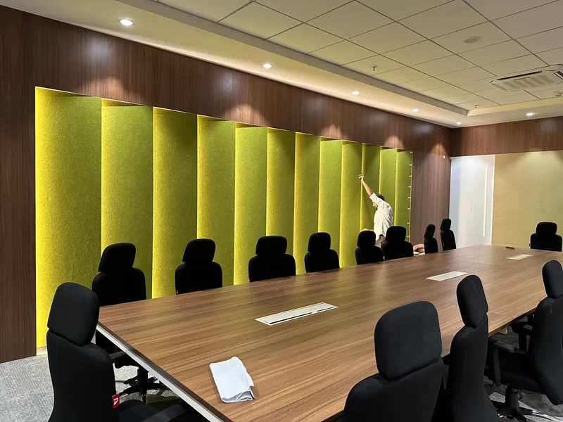 Meeting room with bright green vertical acoustic panel wall and long wooden conference table.