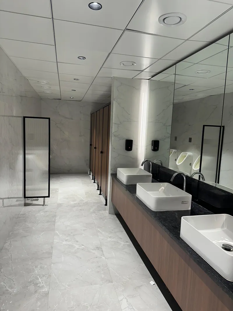 Office restroom with marble walls, vessel basins on stone counter and large mirror.