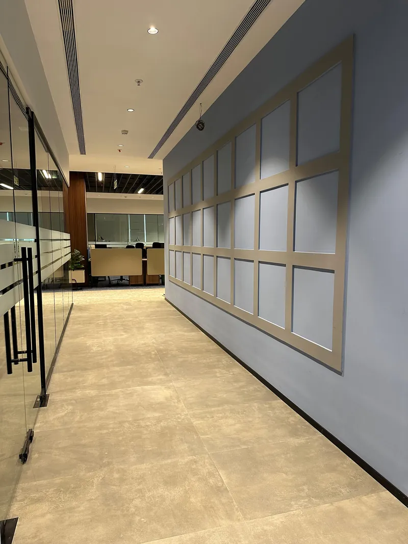 Office corridor with grid-paneled grey feature wall and glass-partitioned meeting room.