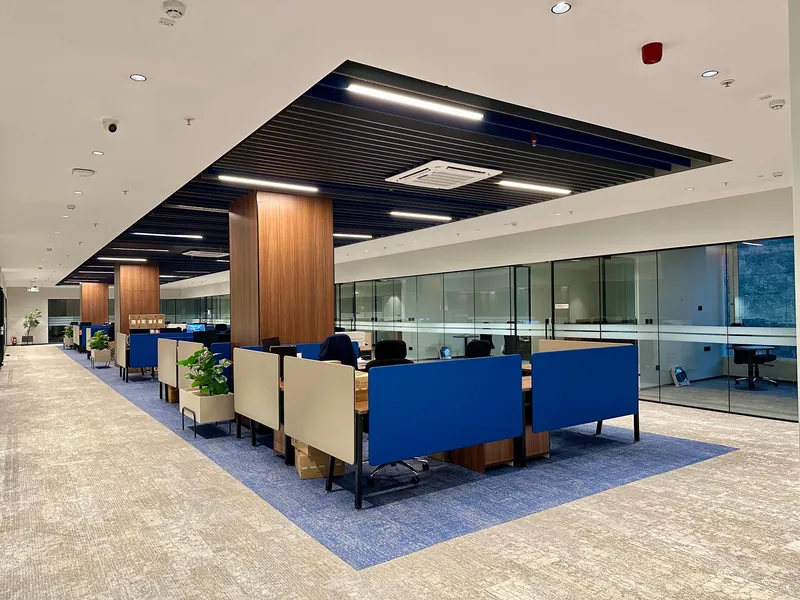 Open office with blue clustered workstations, planters and wood-clad column.