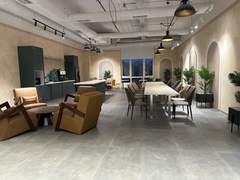 Industrial-style breakout area with meeting table, lounge chairs, and pantry under exposed ceiling.