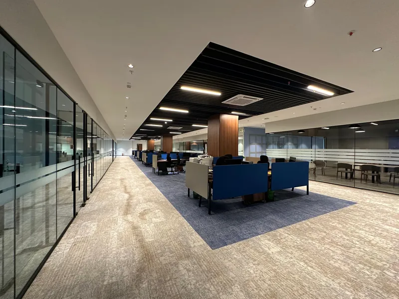 Open-plan office with glass walls, blue lounge seating, and patterned carpet flooring.