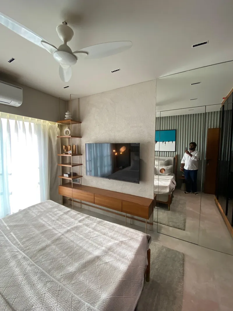 Modern bedroom with TV console, mirrored wardrobe, and textured accent wall.