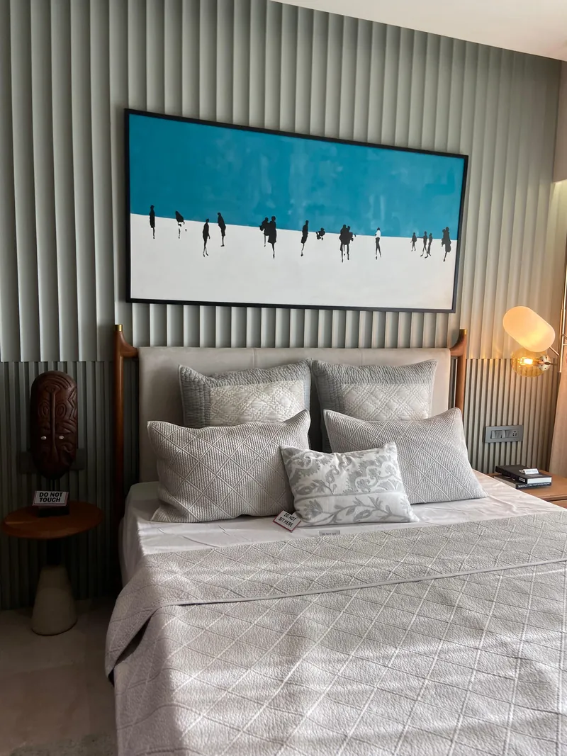 Contemporary bed with fluted wall, blue artwork, and layered grey cushions.