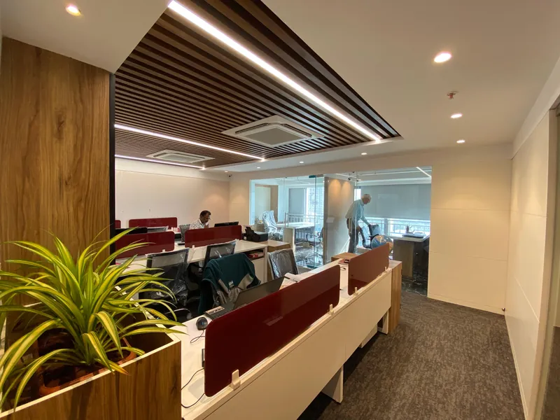 Office workstation rows with red partitions, planter and glass cabin.