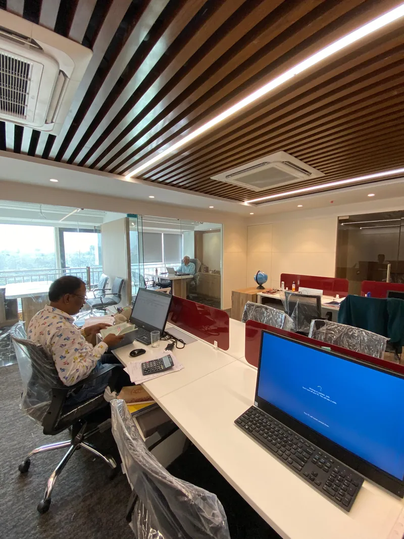 Office desks with monitors below a wooden slat ceiling and glass cabin.