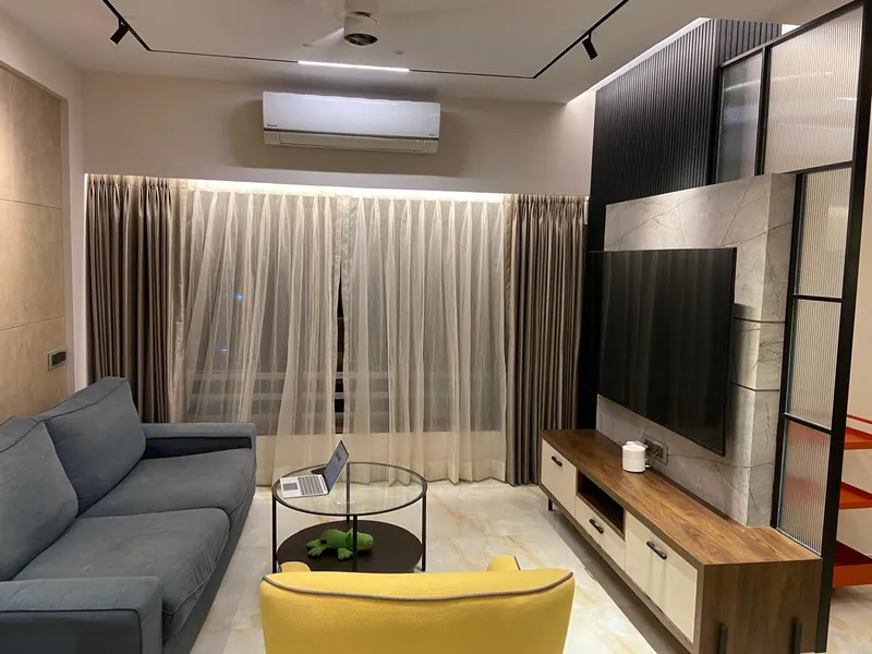 Modern living room with marble TV panel, grey sofa and yellow chair.