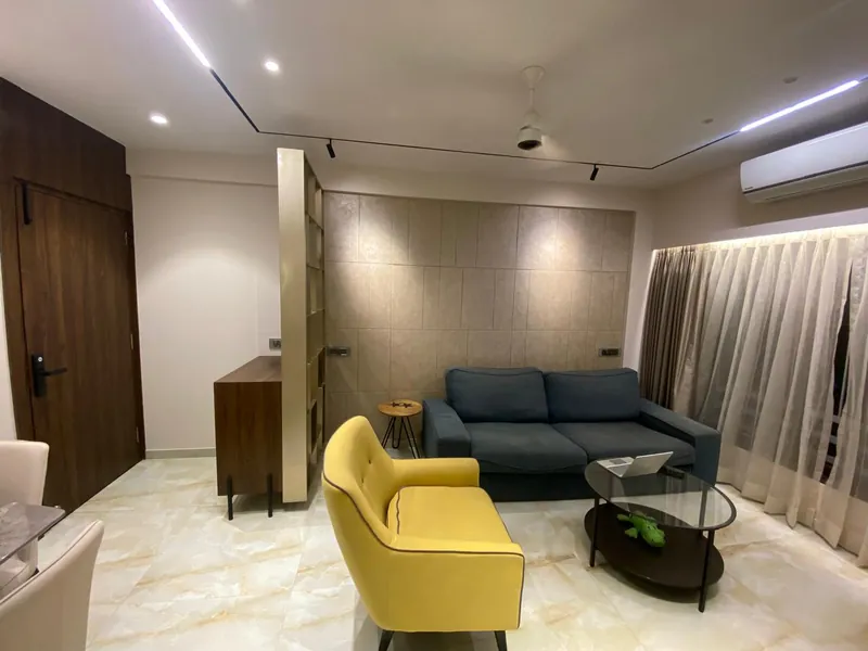 Modern living room with blue sofa, yellow chair and tiled feature wall.