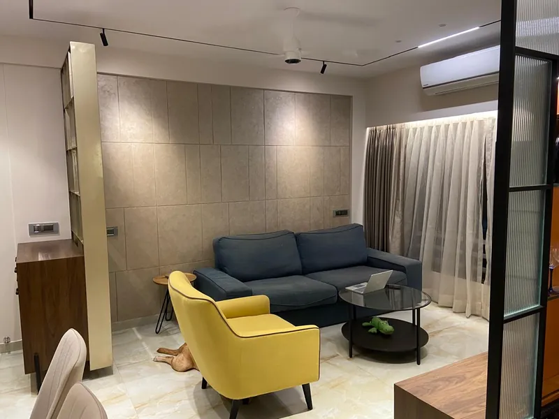 Modern living room with navy sofa, yellow armchair and tiled feature wall.