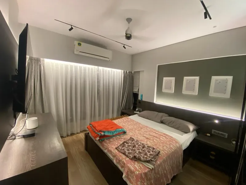 Modern bedroom with upholstered headboard, backlit panels and sheer curtains.