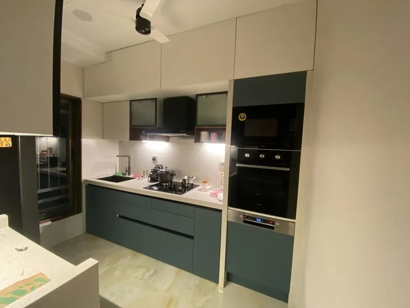 Modern kitchen with green cabinets, built-in oven and white quartz counters.