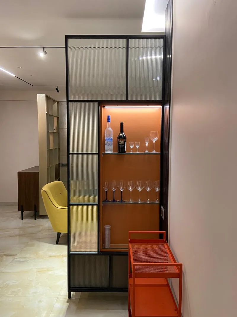 Modern home bar with fluted glass cabinet, glassware and orange bar cart.