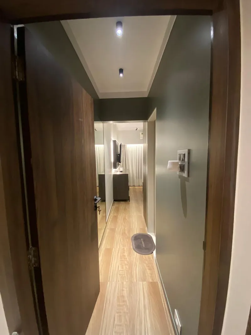 Narrow hallway with wood doors, green wall and wooden flooring leading to bedroom.