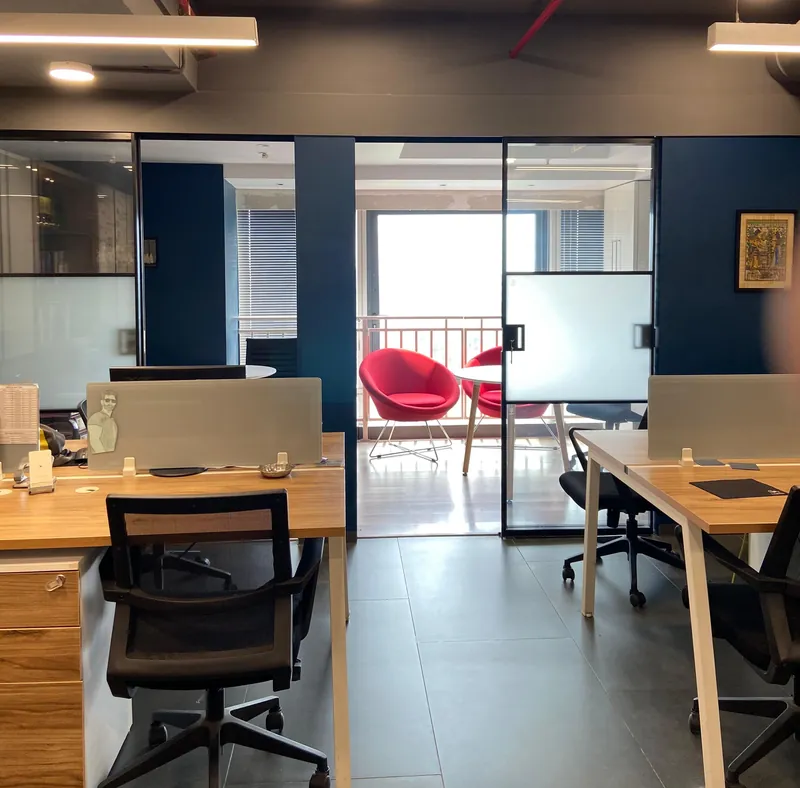 Office workstations with wood desks, mesh chairs and red accent chairs by glass cabin.