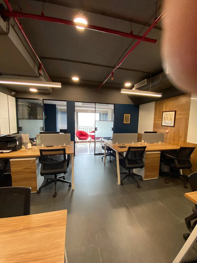 Open office with wood workstations, exposed red piping ceiling and balcony seating.