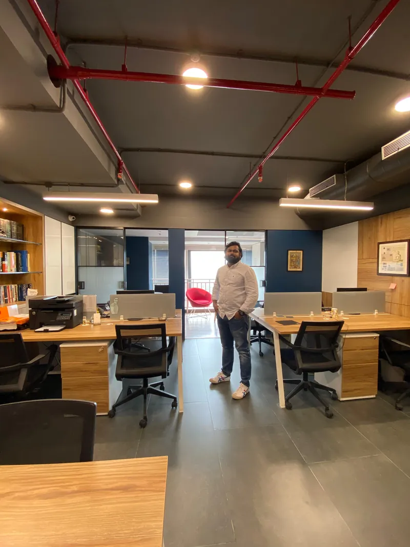 Open-plan office with wood desks, exposed red piping and linear lighting.