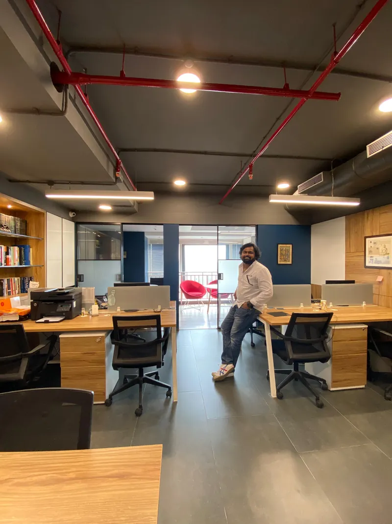 Open office with wood workstations, bookshelf and exposed industrial ceiling.