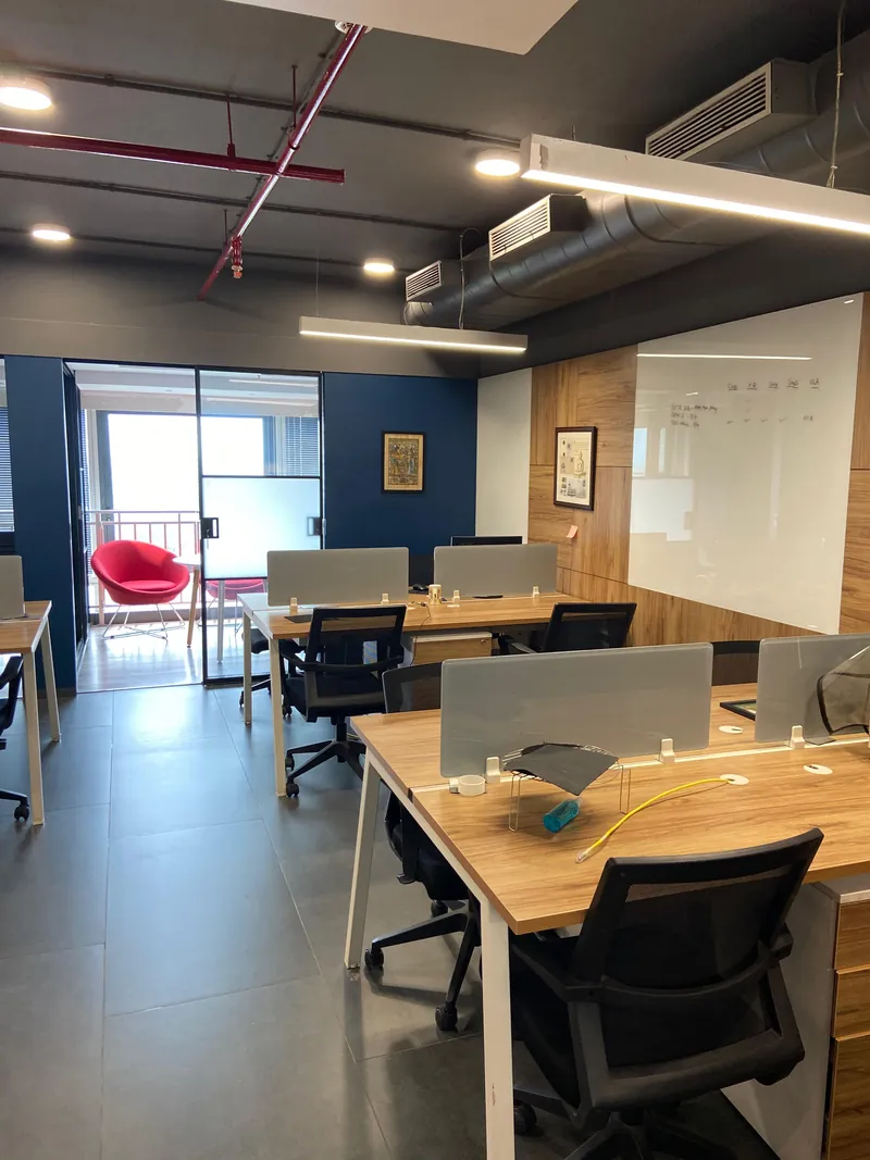 Open-plan office with wooden workstations, black task chairs and exposed ceiling services.