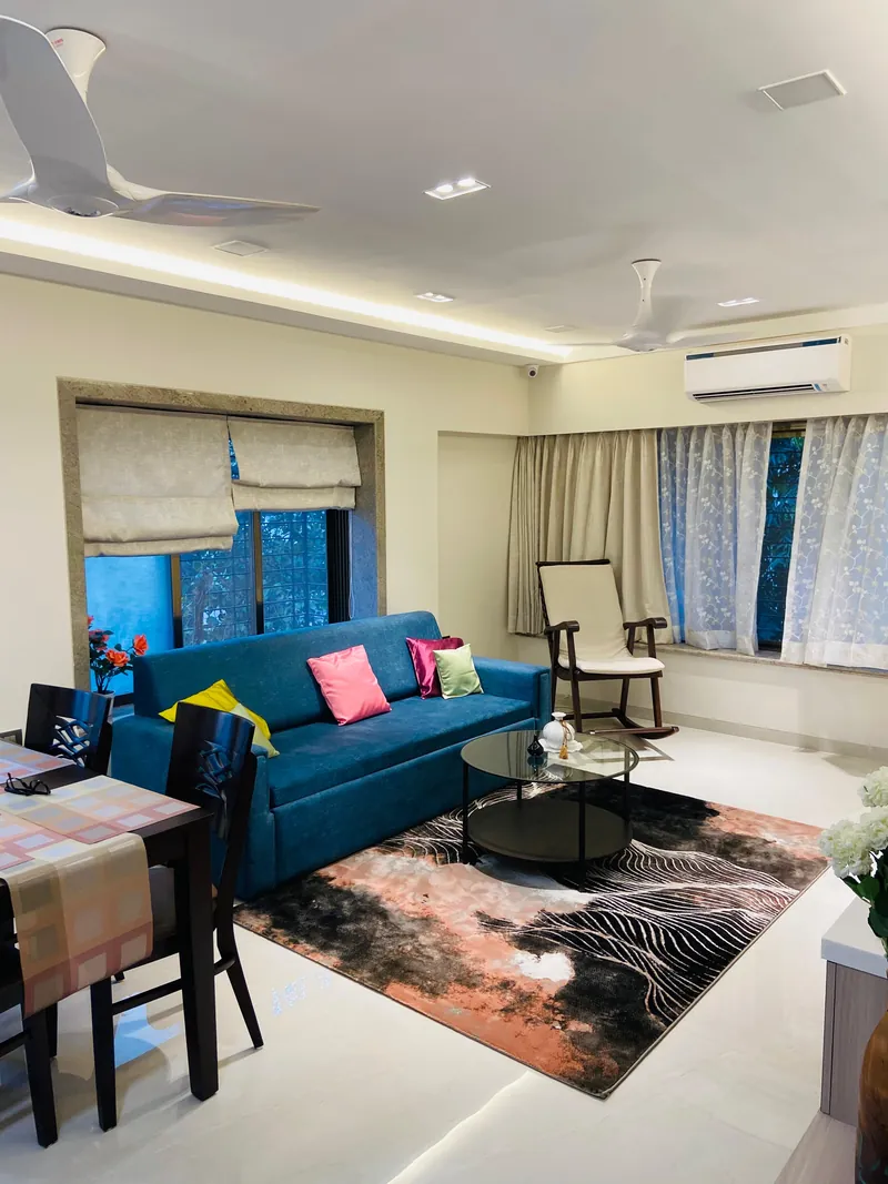 Bright living room with teal sofa, cove lighting and adjacent dining area.