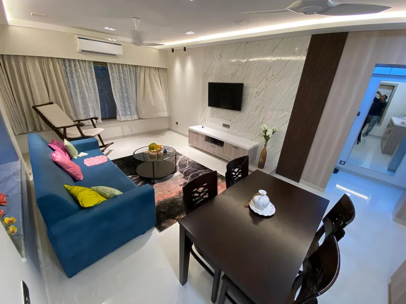Living room with marble TV wall, low console and teal sofa beside dining table.