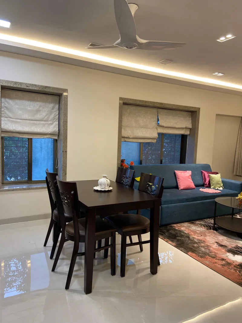 Dining table set near windows with roman blinds and teal sofa behind.