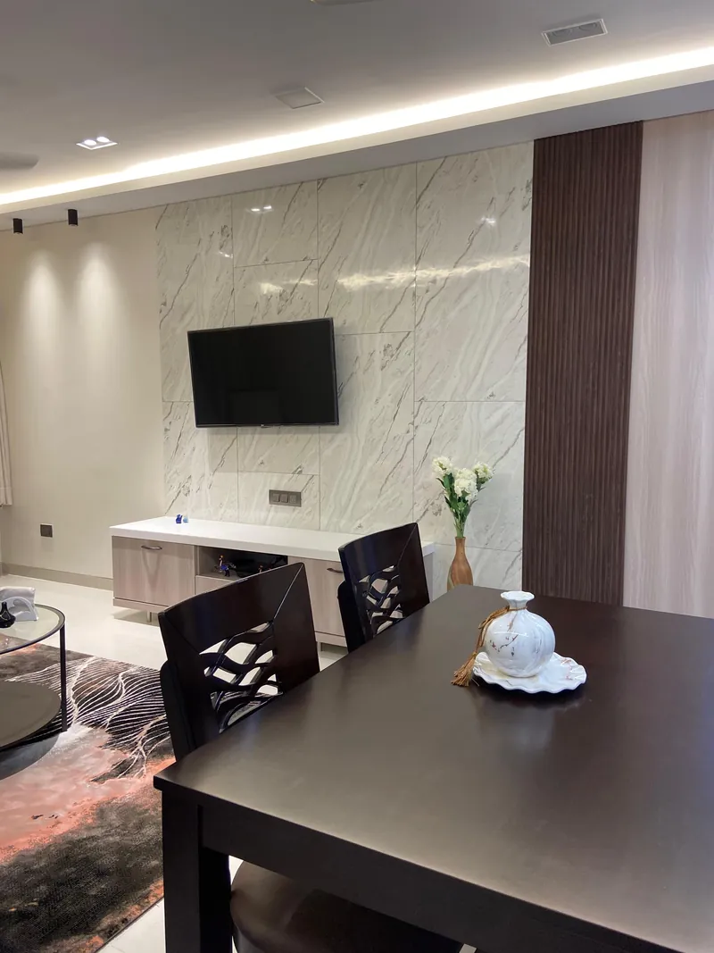 Living area with marble TV wall, low console and dark wood dining table.