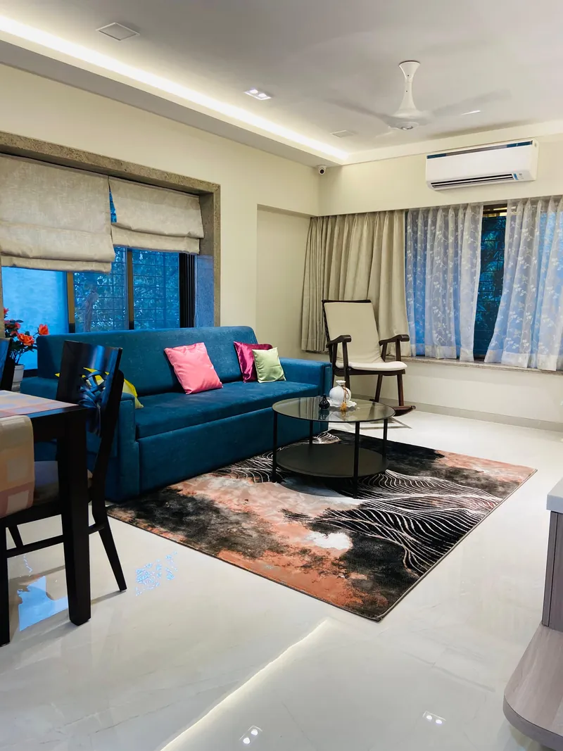 Living room with teal sofa, bright cushions, rocking chair and patterned rug.